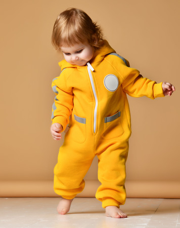 Infant child baby boy kid toddler in yellow  body cloth make first steps happy on light brown backgroundの写真素材