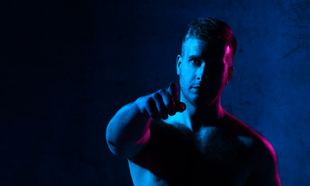 Neon light portrait of sexy smiling man muscular body pointing finger on dark backgroundの写真素材