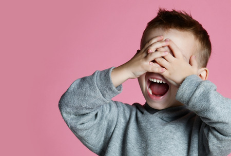 Baby boy kid covering close his eyes with hands and palms screaming laughing  over pink background