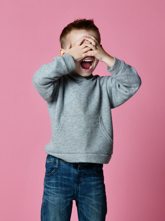 Baby boy kid covering close his eyes with hands and palms screaming laughing  over pink backgroundの写真素材