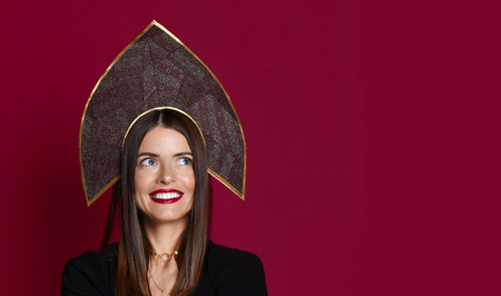 New modern Russian style woman in kokoshnik traditional hat happy smiling looking at the corner with free text space on red backgroundの写真素材