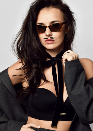 Portrait of brunette woman with mustaches in new modern brown fashion sunglasses on gray backgroundの写真素材