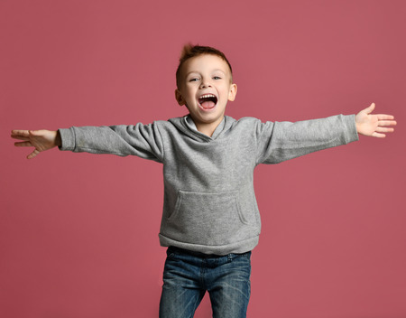 Young boy kid jumping in grey hoodie with hands spread up laughing smiling on pink backgroundの写真素材