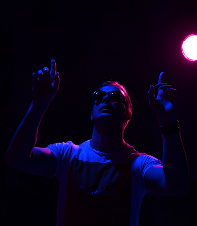 Neon light portrait of sexy brutal man muscular body in white sunglasses on dark background looking  pointing fingers upの写真素材