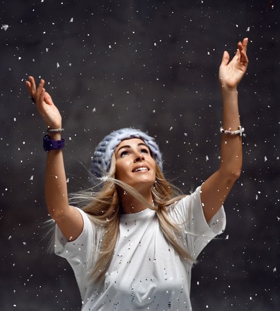 Blonde woman in light blue knitted hat happy smiling sitting under snowflakes winter time conceptの写真素材