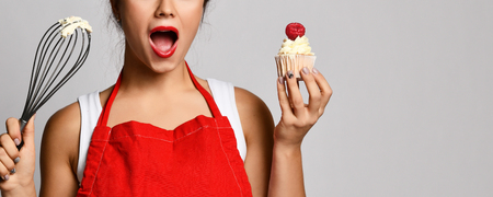 Young woman chef cook preparing sweet cup cake with cream surprised on gray backgroundの写真素材