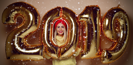 Woman celebrating New Year xmas party happy laughing in yellow sweater blouse with 2019 gold balloons on beige backgroundの写真素材