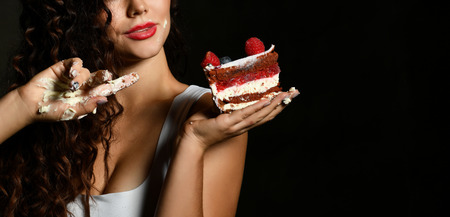 Young woman chef cook holding sweet piece cake with strawberry blueberry and cream smiling on black...