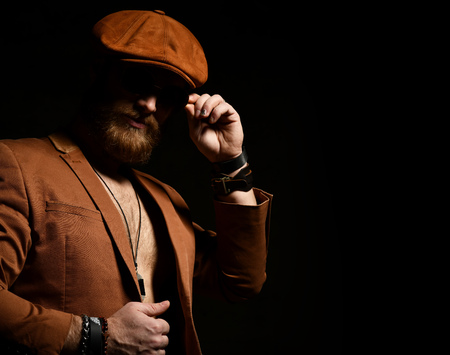 Brutal business man with beard and mustache in  brown cap and jacket on dark backgroundの写真素材