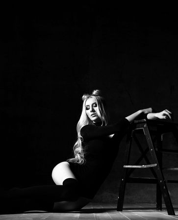 Young sexy blonde fashion woman sitting on floor in black body dress on dark night background black and white pictureの写真素材