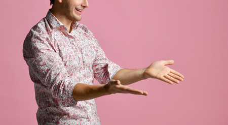 Young man in shirt have a dialog gesticulating with open hands palms smiling on modern pink backgroundの写真素材