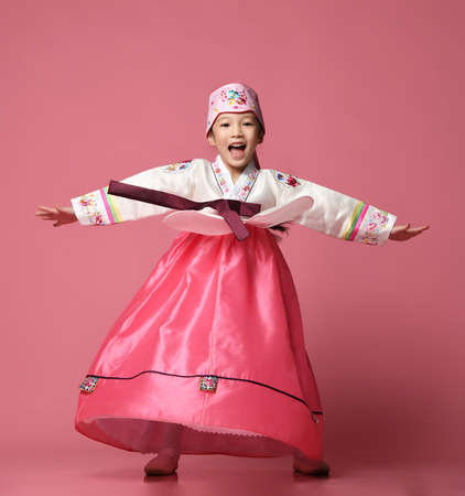 Korean little baby girl in traditional silk dress for new year celebration dancing on pink background with hands spreadの写真素材