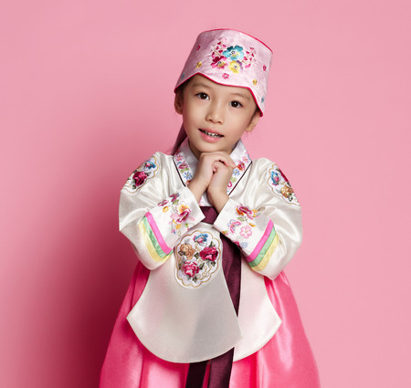 Korean little baby girl in traditional silk dress for new year celebration on pink background with hands in pray signの写真素材