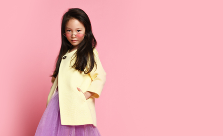 Little asian girl in yellow fashion jacket purple dress and modern red sunglasses posing on pink backgroundの写真素材