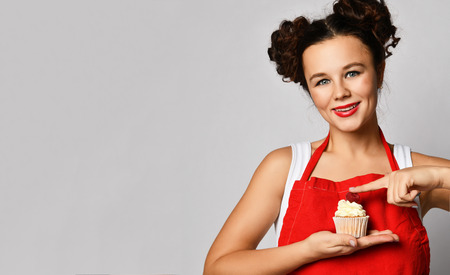 Young woman chef cook preparing sweet cup cake with cream and raspberry happy smiling on gray backgroundの写真素材
