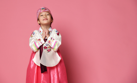 Korean little baby girl in traditional silk dress for new year celebration on pink background with hands spreadの写真素材