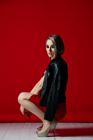 Beautiful sexy woman in black modern stylish jacket casual skirt and bra underwear red lipstick  on red background looking at the cornerの写真素材