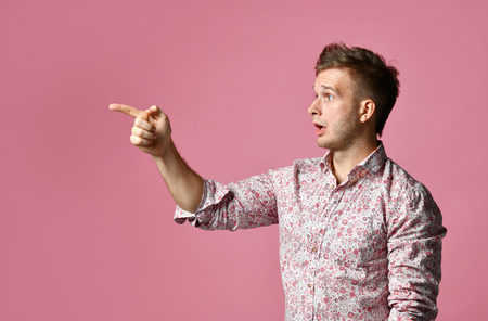 Young happy man in shirt surprised pointing finger hand gesticulate on pink backgroundの写真素材
