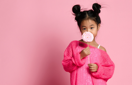 Happy young asian little girl kid lick eat happy big sweet lollypop candy on pink backgroundの写真素材