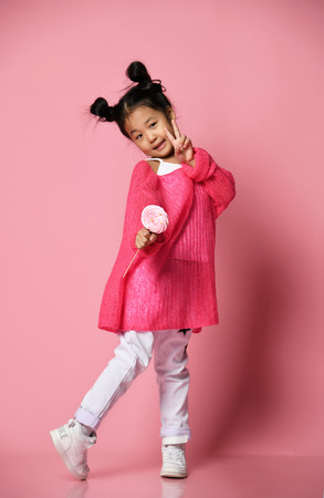 Happy young asian little girl kid lick eat happy big sweet lollypop candy on pink backgroundの写真素材