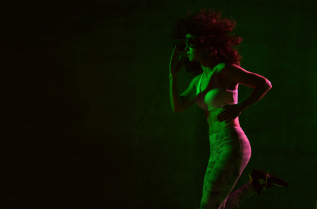 Young sport woman with afro hairstyle running jogging in gyn in green and pink neon light on dark wall backgroundの写真素材