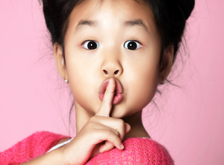 Asian kid girl in pink sweater shows shhh quiet sign on pink backgroundの写真素材