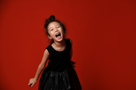 Young asian Korean girl in black trendy dress happy shouting screaming on red background
