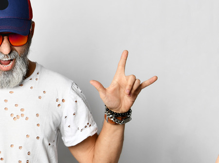 Old brutal in designer t-shirt, blue jeans and baseball cap shows rock'n'roll and shouts stylish fashionable men isolated on whiteの写真素材