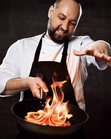 Professional chef prepares the dish with flame stirring in a frying pan on kitchen of the restaurant. Cooking tasty meal over an open fireの写真素材
