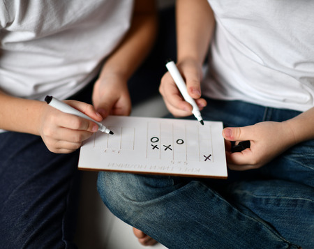 two kids boy and girl in white t-shirts and blue jeans sit close to each other and play cross-zero on white wooden floorの写真素材