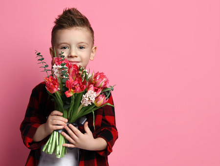 Nice little boy kid in red shirt with a big bouquet of spring flowers ready to congratulate with a...