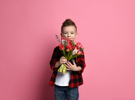 Nice little boy kid in red shirt with holds gently a bouquet of flowers and is ready to congratulate...