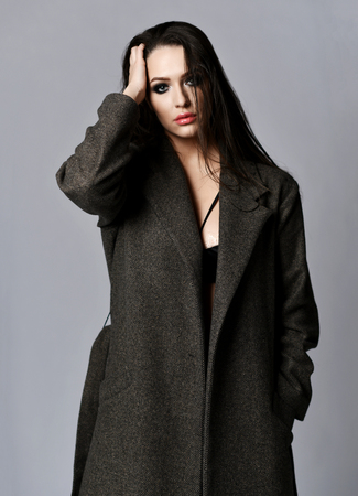 Closeup portrait of young beautiful woman posing in long sexy spring jacket and underwear on gray backgroundの写真素材
