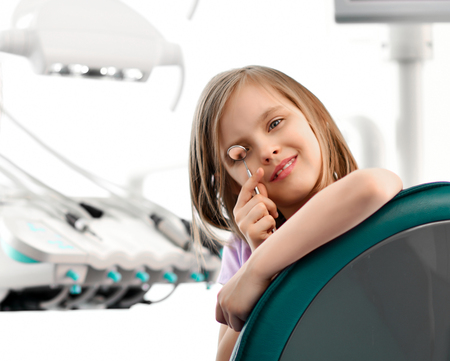 Kid girl in a big dental chair plays with dental mirrorの写真素材