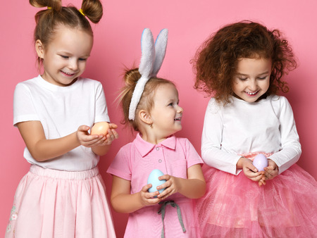 Three laughting kid girls happy to get painted eggs on Easter day. Happy Easter concept holiday celebration on pink backgroundの写真素材