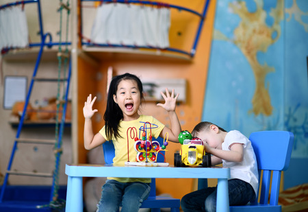 Two joyful  kids preschoolers boy and girl play enthusiastically at the table with toys on playroom backgroundの写真素材