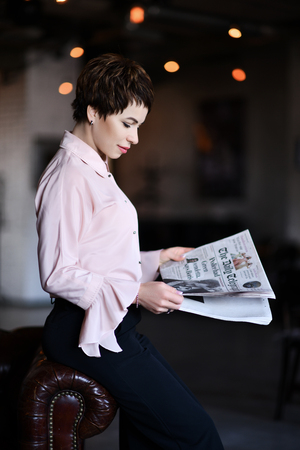 Business woman in modern fashion official suit reads a business news papers during her break on background of modern officeの写真素材