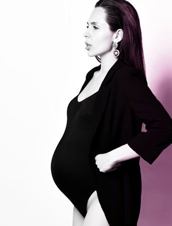 Pregnancy, maternity, preparation and expectation concept. Beautiful fashion pregnant woman holds hands on belly waiting for birth of little child on gray backgroundの写真素材