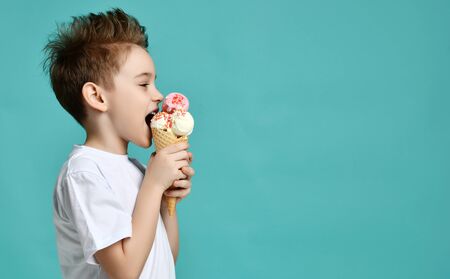 Baby boy kid eat raspberry and vanilla ice-cream in waffles cone on blue mint background with free text copy spaceの写真素材