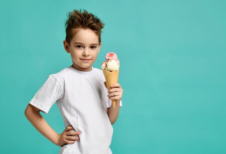 Baby boy kid hold three scoops of strawberry and vanilla ice cream in waffles cone on blue mint background with free text copy spaceの写真素材
