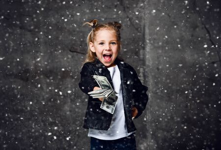 Happy screaming rich kid girl millionaire in leather jacket is handing us, giving, holding in hand a...