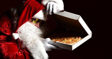 Santa Claus in sunglasses lifting the pizza box lid and peering inside, watching, desiring, going to steal a slice piece. New year and Merry Christmas fast food concept bannerの写真素材