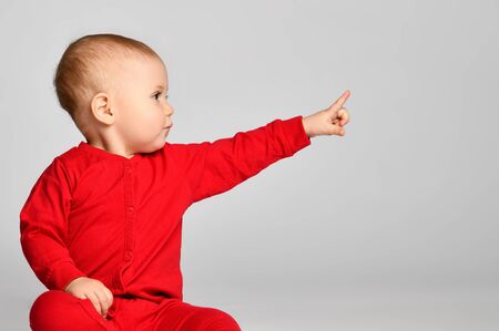 Little toddler boy points finger up side in red infant bodysuit with free text space on gray backgroundの写真素材