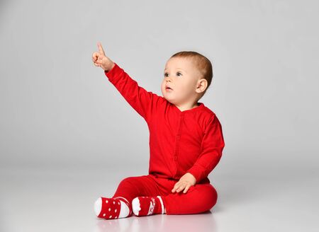 Little toddler boy points finger up side in red infant bodysuit with free text space on gray background full bodyの写真素材