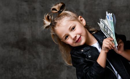 Happy screaming rich kid girl lucky millionaire in leather jacket is holding a bundle of moneyの写真素材