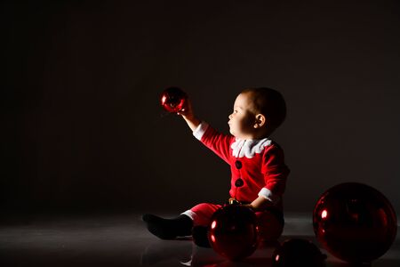 Little child boy toddler in santa claus costume surrounded by christmas tree red glass ballsの写真素材