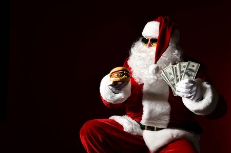 Happy Santa Claus in stylish sunglasses offer tasty burger sandwich hamburger in hand. New year and Merry Christmas fast food conceptの写真素材