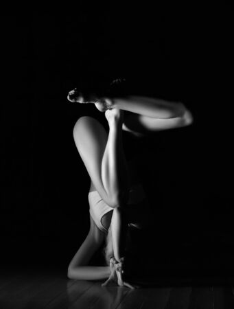 Sporty girl trainer doing yoga asana difficult pose stretches in sport fitness gym club in sportswear on dark gym background. Black and white imageの写真素材