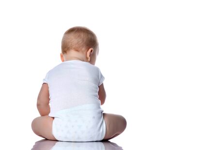 Infant child baby boy toddler in white bodysuit with copyspace blank is sitting with his back to us on white background with free text copy spaceの写真素材