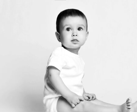 Black and white portrait in profile of calm infant baby boy toddler in white bodysuit sitting...